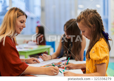 Creative kids during an art class in a daycare center or elementary school classroom drawing with female teacher. 121336279