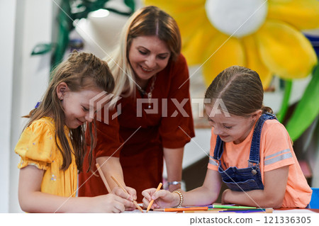 Creative kids during an art class in a daycare center or elementary school classroom drawing with female teacher. Creative kids during an art class in a daycare center or elementary school classroom drawing with female teacher. 121336305
