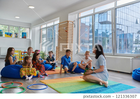 Reading time in an elementary school or kindergarten, a teacher reads a book to children in an elementary school or kindergarten. The concept of pre-school education. Selective focus 121336307