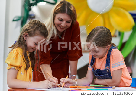 Creative kids during an art class in a daycare center or elementary school classroom drawing with female teacher. Creative kids during an art class in a daycare center or elementary school classroom drawing with female teacher. 121336309