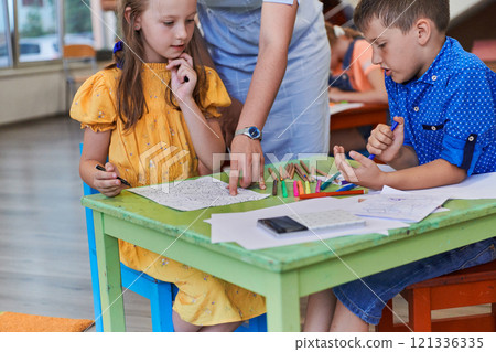 Creative kids during an art class in a daycare center or elementary school classroom drawing with female teacher. 121336335