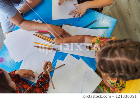 Creative kids during an art class in a daycare center or elementary school classroom drawing with female teacher. 121336351
