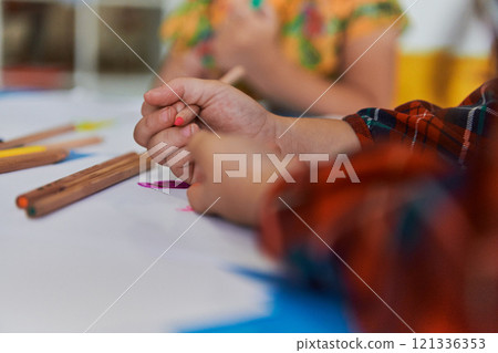 Close up photo of kids during an art class in a daycare center or elementary school classroom drawing with female teacher. 121336353