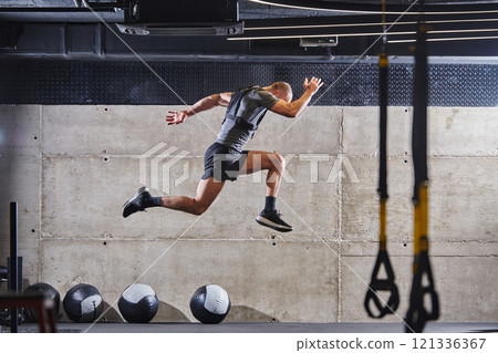 A muscular man captured in air as he jumps in a modern gym, showcasing his athleticism, power, and determination through a highintensity fitness routine A muscular man captured in air as he jumps in a modern gym, showcasing his athleticism, power, and determination through a highintensity fitness routine 121336367