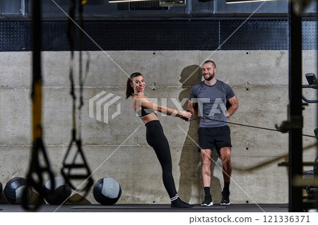 A muscular man assisting a fit woman in a modern gym as they engage in various body exercises and muscle stretches, showcasing their dedication to fitness and benefiting from teamwork and support A muscular man assisting a fit woman in a modern gym as they engage in various body exercises and muscle stretches, showcasing their dedication to fitness and benefiting from teamwork and support 121336371