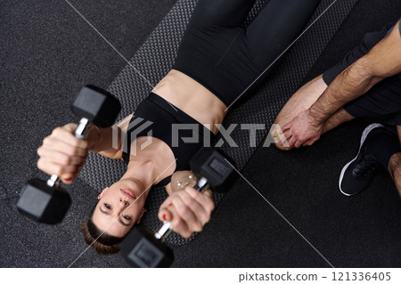A muscular man assisting a fit woman in a modern gym as they engage in various body exercises and muscle stretches, showcasing their dedication to fitness and benefiting from teamwork and support A muscular man assisting a fit woman in a modern gym as they engage in various body exercises and muscle stretches, showcasing their dedication to fitness and benefiting from teamwork and support 121336405