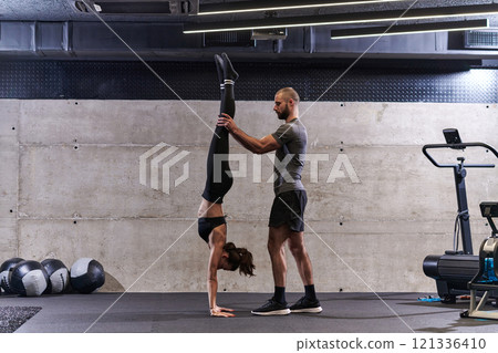 A muscular man assisting a fit woman in a modern gym as they engage in various body exercises and muscle stretches, showcasing their dedication to fitness and benefiting from teamwork and support A muscular man assisting a fit woman in a modern gym as they engage in various body exercises and muscle stretches, showcasing their dedication to fitness and benefiting from teamwork and support 121336410