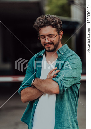A successful young businessman in a shirt, with crossed arms, poses outdoors, confident expression on his face. A successful young businessman in a shirt, with crossed arms, poses outdoors, confident expression on his face. 121336434