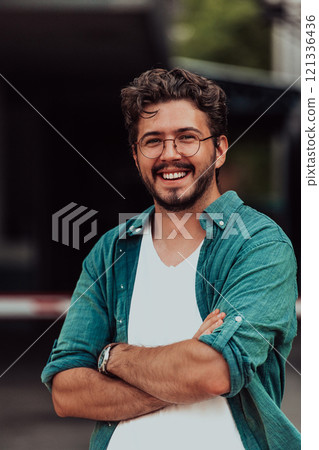 A successful young businessman in a shirt, with crossed arms, poses outdoors, confident expression on his face. 121336436
