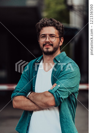 A successful young businessman in a shirt, with crossed arms, poses outdoors, confident expression on his face. A successful young businessman in a shirt, with crossed arms, poses outdoors, confident expression on his face. 121336560