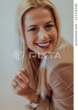 A confident and successful businesswoman, with a wide smile, strikes a pose in front of a beige background, exuding professionalism and elegance 121336580