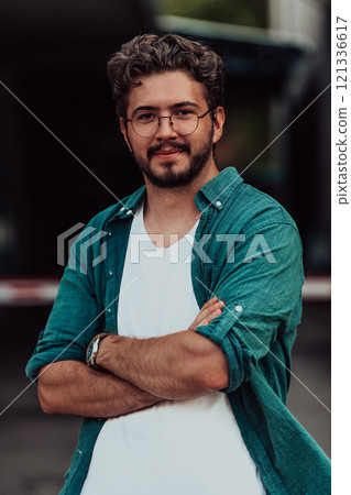 A successful young businessman in a shirt, with crossed arms, poses outdoors, confident expression on his face. 121336617