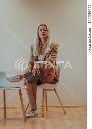 A professional businesswoman sits on a chair, surrounded by a serene beige background, diligently working on her laptop, showcasing dedication and focus in her pursuit of success A professional businesswoman sits on a chair, surrounded by a serene beige background, diligently working on her laptop, showcasing dedication and focus in her pursuit of success 121336662