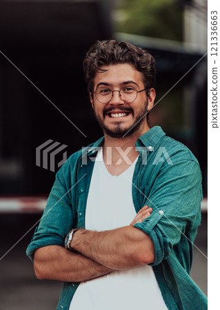 A successful young businessman in a shirt, with crossed arms, poses outdoors, confident expression on his face. 121336663