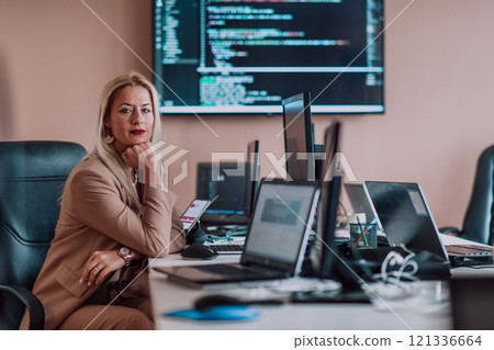 A businesswoman sitting in a programmer's office surrounded by computers, showing her expertise and dedication to technology. 121336664