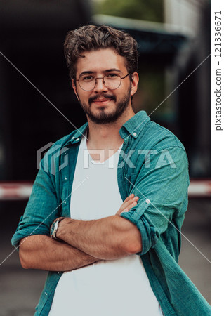 A successful young businessman in a shirt, with crossed arms, poses outdoors, confident expression on his face. 121336671