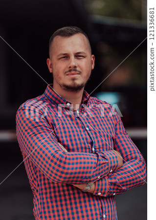 A successful young businessman in a shirt, with crossed arms, poses outdoors, confident expression on his face. A successful young businessman in a shirt, with crossed arms, poses outdoors, confident expression on his face. 121336681