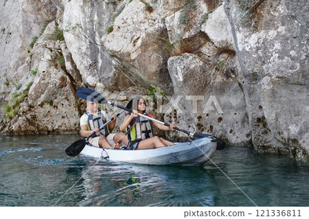 A young couple enjoying an idyllic kayak ride in the middle of a beautiful river surrounded by forest greenery 121336811