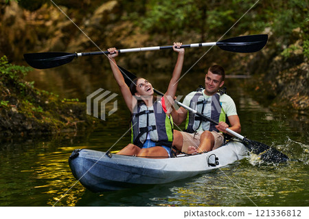 A young couple enjoying an idyllic kayak ride in the middle of a beautiful river surrounded by forest greenery 121336812