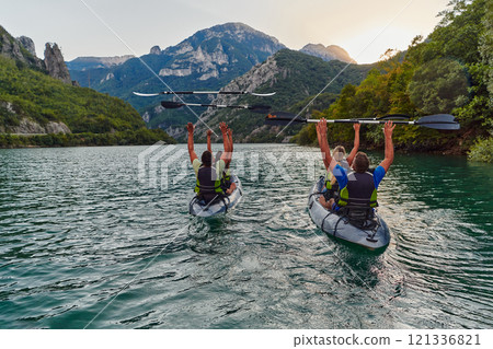 A group of friends enjoying fun and kayaking exploring the calm river, surrounding forest and large natural river canyons during an idyllic sunset. A group of friends enjoying fun and kayaking exploring the calm river, surrounding forest and large natural river canyons during an idyllic sunset. 121336821