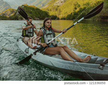 A young couple enjoying an idyllic kayak ride in the middle of a beautiful river surrounded by forest greenery 121336850