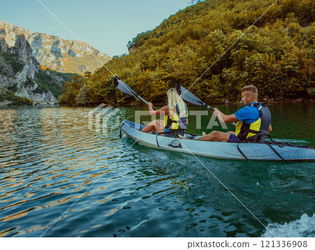 A young couple enjoying an idyllic kayak ride in the middle of a beautiful river surrounded by forest greenery 121336908