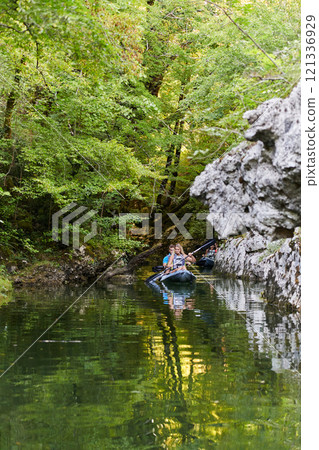 A group of friends enjoying having fun and kayaking while exploring the calm river, surrounding forest and large natural river canyons A group of friends enjoying having fun and kayaking while exploring the calm river, surrounding forest and large natural river canyons 121336929