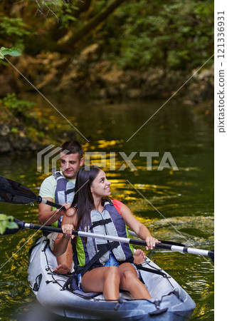 A young couple enjoying an idyllic kayak ride in the middle of a beautiful river surrounded by forest greenery 121336931