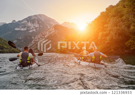 A group of friends enjoying fun and kayaking exploring the calm river, surrounding forest and large natural river canyons during an idyllic sunset. 121336933