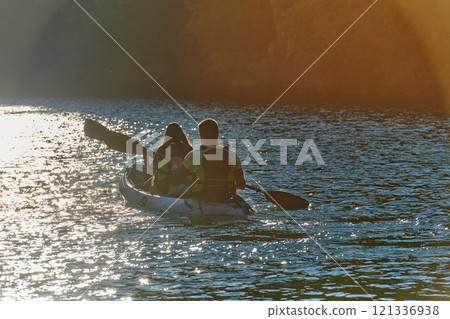 A young couple enjoying an idyllic kayak ride in the middle of a beautiful river surrounded by forest greenery in sunset time A young couple enjoying an idyllic kayak ride in the middle of a beautiful river surrounded by forest greenery in sunset time 121336938