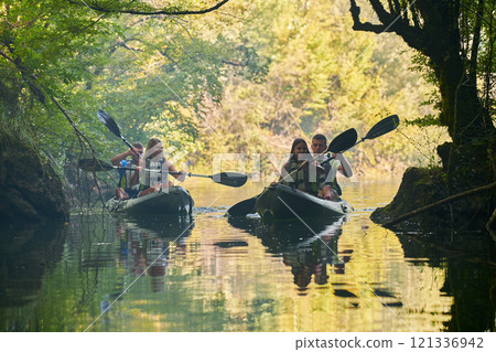 A group of friends enjoying having fun and kayaking while exploring the calm river, surrounding forest and large natural river canyons A group of friends enjoying having fun and kayaking while exploring the calm river, surrounding forest and large natural river canyons 121336942