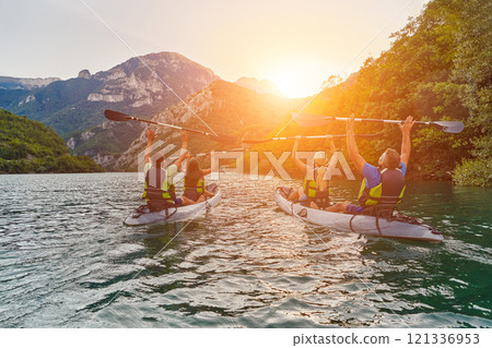 A group of friends enjoying fun and kayaking exploring the calm river, surrounding forest and large natural river canyons during an idyllic sunset. 121336953