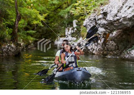 A young couple enjoying an idyllic kayak ride in the middle of a beautiful river surrounded by forest greenery 121336955