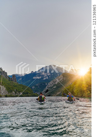 A group of friends enjoying fun and kayaking exploring the calm river, surrounding forest and large natural river canyons during an idyllic sunset. 121336965