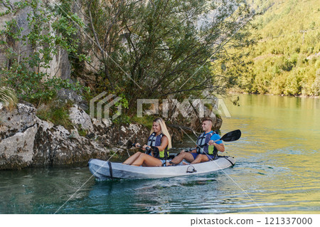 A young couple enjoying an idyllic kayak ride in the middle of a beautiful river surrounded by forest greenery 121337000