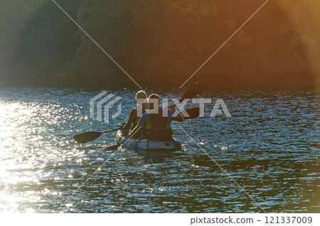 A young couple enjoying an idyllic kayak ride in the middle of a beautiful river surrounded by forest greenery in sunset time  121337009