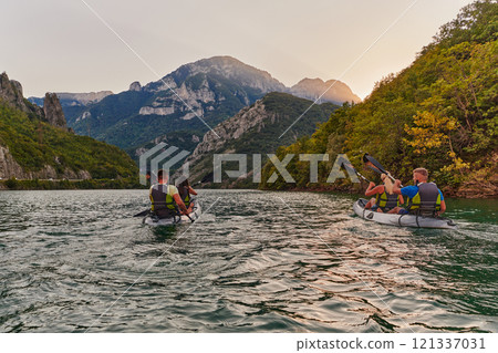 A group of friends enjoying fun and kayaking exploring the calm river, surrounding forest and large natural river canyons during an idyllic sunset. 121337031