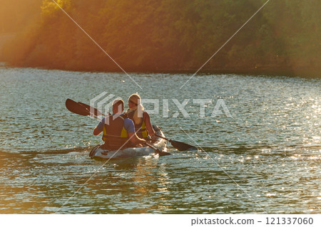 A young couple enjoying an idyllic kayak ride in the middle of a beautiful river surrounded by forest greenery in sunset time  121337060