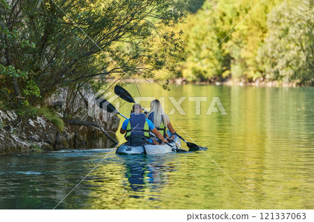 A young couple enjoying an idyllic kayak ride in the middle of a beautiful river surrounded by forest greenery 121337063