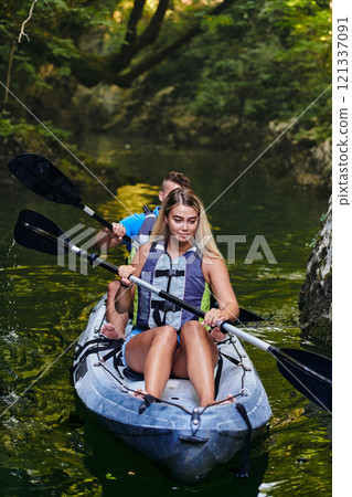 A young couple enjoying an idyllic kayak ride in the middle of a beautiful river surrounded by forest greenery 121337091
