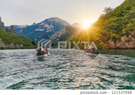 A group of friends enjoying fun and kayaking exploring the calm river, surrounding forest and large natural river canyons during an idyllic sunset. 121337098