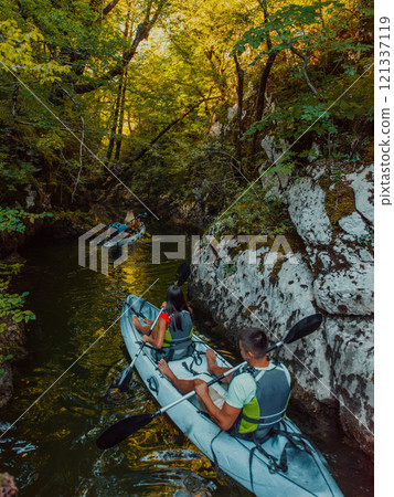 A young couple enjoying an idyllic kayak ride in the middle of a beautiful river surrounded by forest greenery 121337119