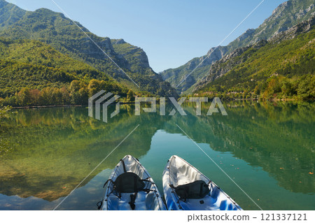 An idyllic photo of two kayaks on the river bank. In the background of green forest area and mountains An idyllic photo of two kayaks on the river bank. In the background of green forest area and mountains 121337121