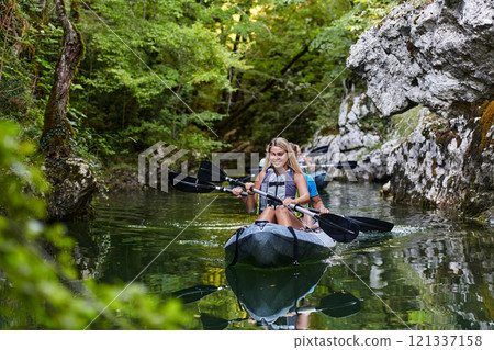 A young couple enjoying an idyllic kayak ride in the middle of a beautiful river surrounded by forest greenery 121337158