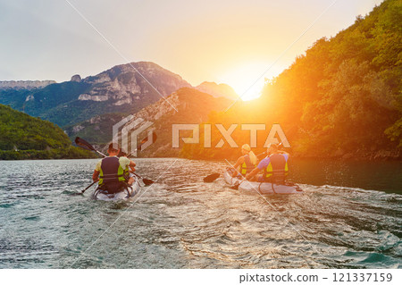 A group of friends enjoying fun and kayaking exploring the calm river, surrounding forest and large natural river canyons during an idyllic sunset. 121337159