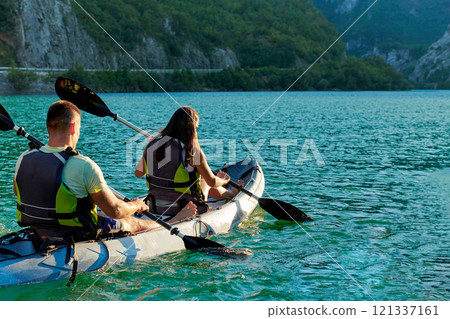 A young couple enjoying an idyllic kayak ride in the middle of a beautiful river surrounded by forest greenery in sunset time  121337161