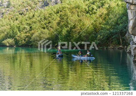 A group of friends enjoying fun and kayaking exploring the calm river, surrounding forest and large natural river canyons during an idyllic sunset. 121337168