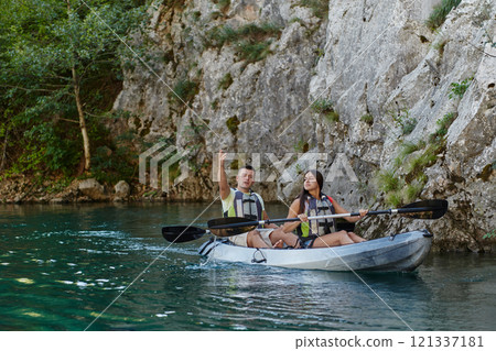 A young couple enjoying an idyllic kayak ride in the middle of a beautiful river surrounded by forest greenery A young couple enjoying an idyllic kayak ride in the middle of a beautiful river surrounded by forest greenery 121337181