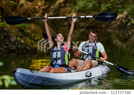A young couple enjoying an idyllic kayak ride in the middle of a beautiful river surrounded by forest greenery 121337186