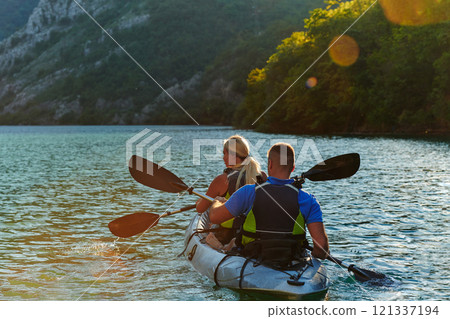 A young couple enjoying an idyllic kayak ride in the middle of a beautiful river surrounded by forest greenery in sunset time A young couple enjoying an idyllic kayak ride in the middle of a beautiful river surrounded by forest greenery in sunset time 121337194
